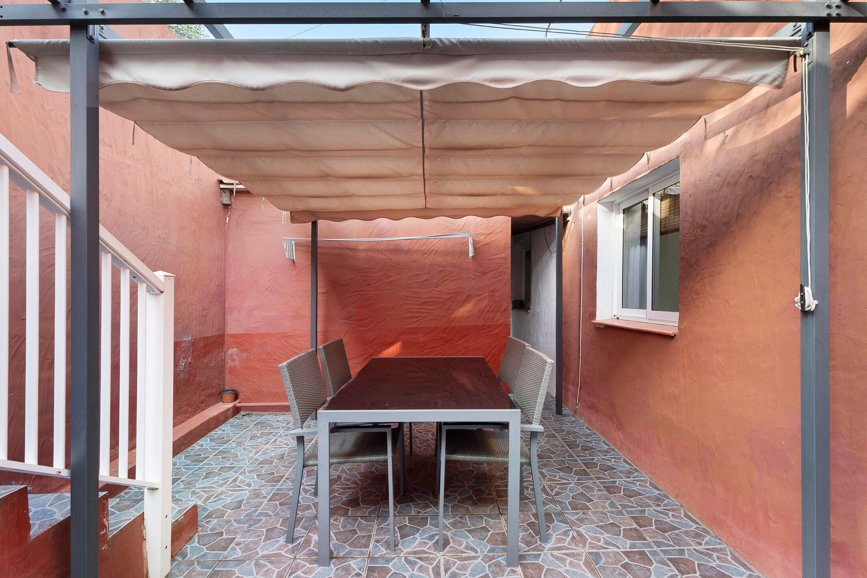 A covered patio with a table and chairs, a window, and a red wall.
