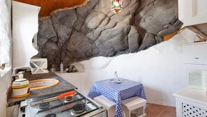 Een keuken met een gasfornuis, een spoelbak, een tafel met een blauw geruit tafelkleed en een stenen muur.