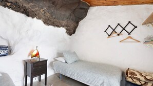 Een knus slaapkamer met een enkel bed, een nachtkastje met lamp, een hanglamp en een kapstok aan de muur.