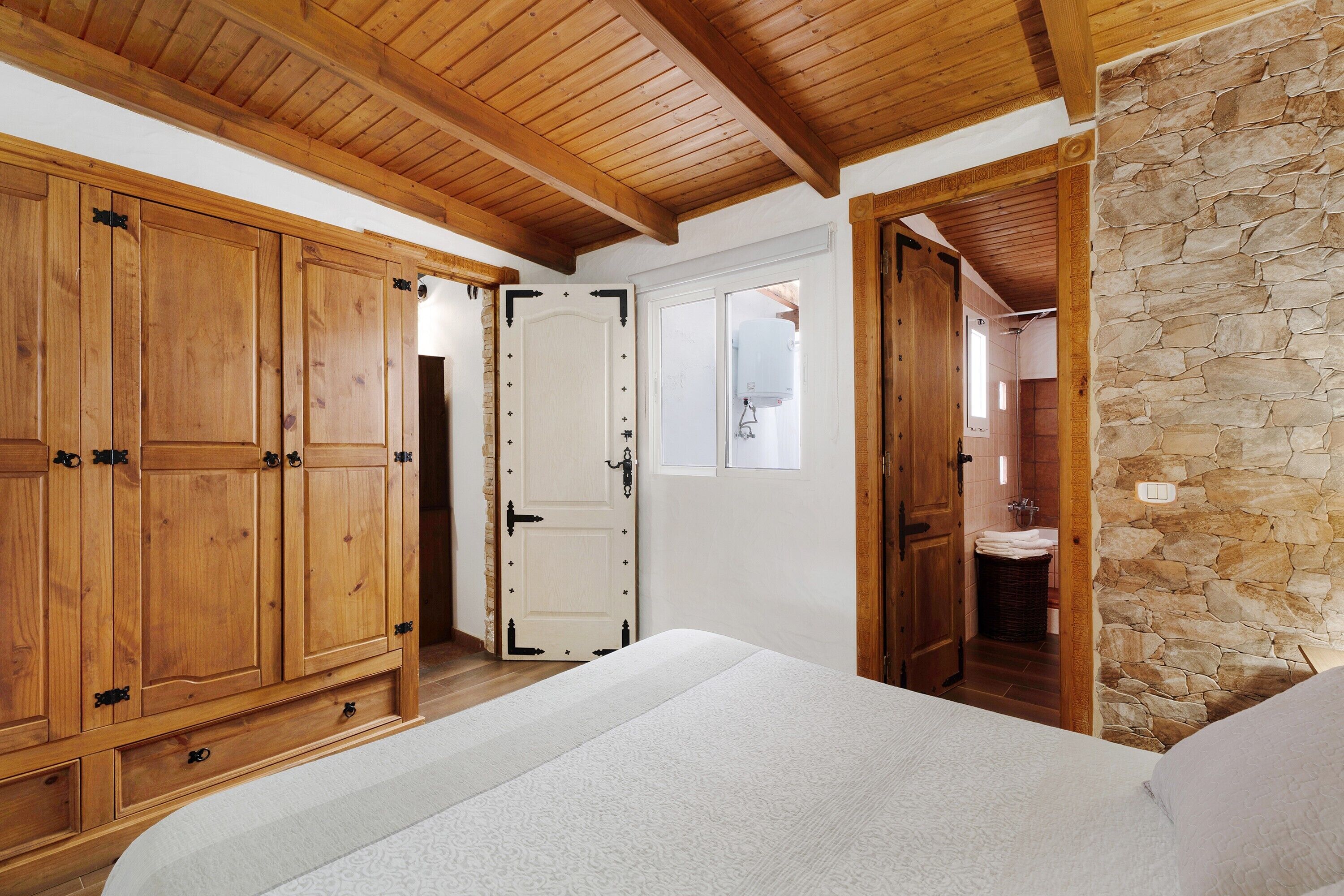Un dormitorio con muebles de madera, una pared de piedra y una puerta que da a un baño.