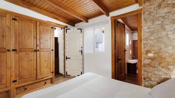 Un dormitorio con muebles de madera, una pared de piedra y una puerta que da a un baño.