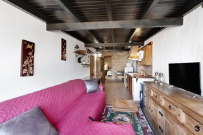Sala de estar con un sofá rosa, armarios de madera, un televisor y una cocina al fondo.