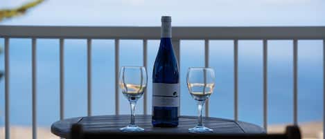 A table with a bottle and two glasses on a balcony with a railing.