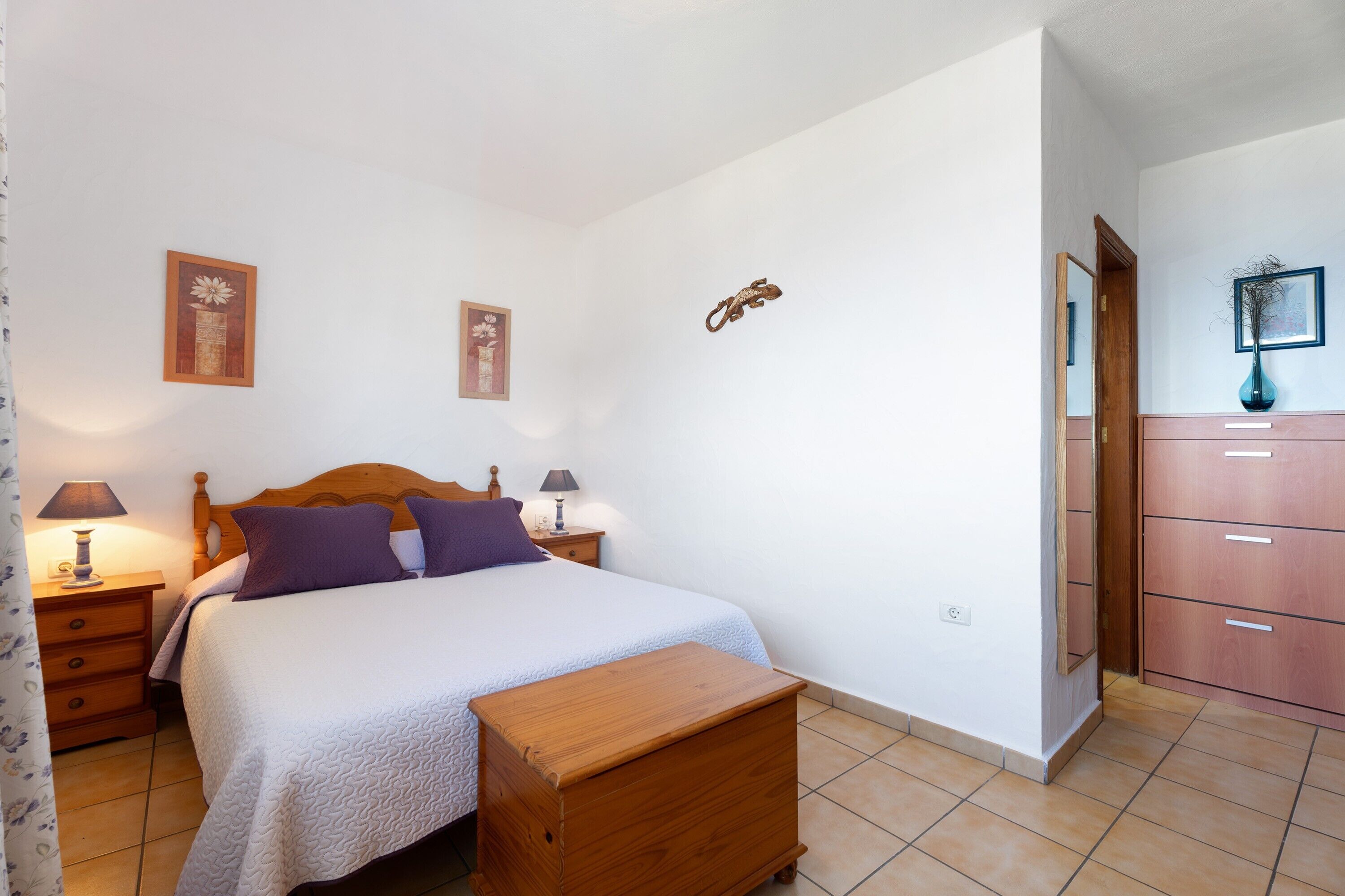 A bedroom with a bed, bedside tables, a wooden bench, a wardrobe, and a mirror.