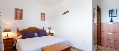 A bedroom with a bed, bedside tables, a wooden bench, a wardrobe, and a mirror.
