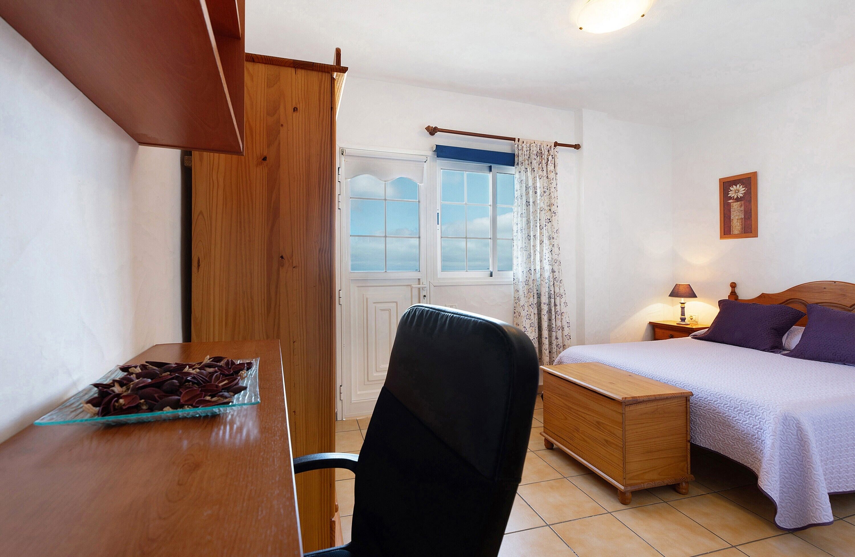Une chambre à coucher avec un lit, une table de chevet, une lampe et une fenêtre avec des rideaux.