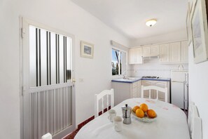A kitchen with white cabinets, a dining table with a white tablecloth, and a window with blinds. - Holiday Home 'El Puerto De La Estaca 3' with Sea View, Private Garden and Balcony (Santa Cruz de Tenerife)