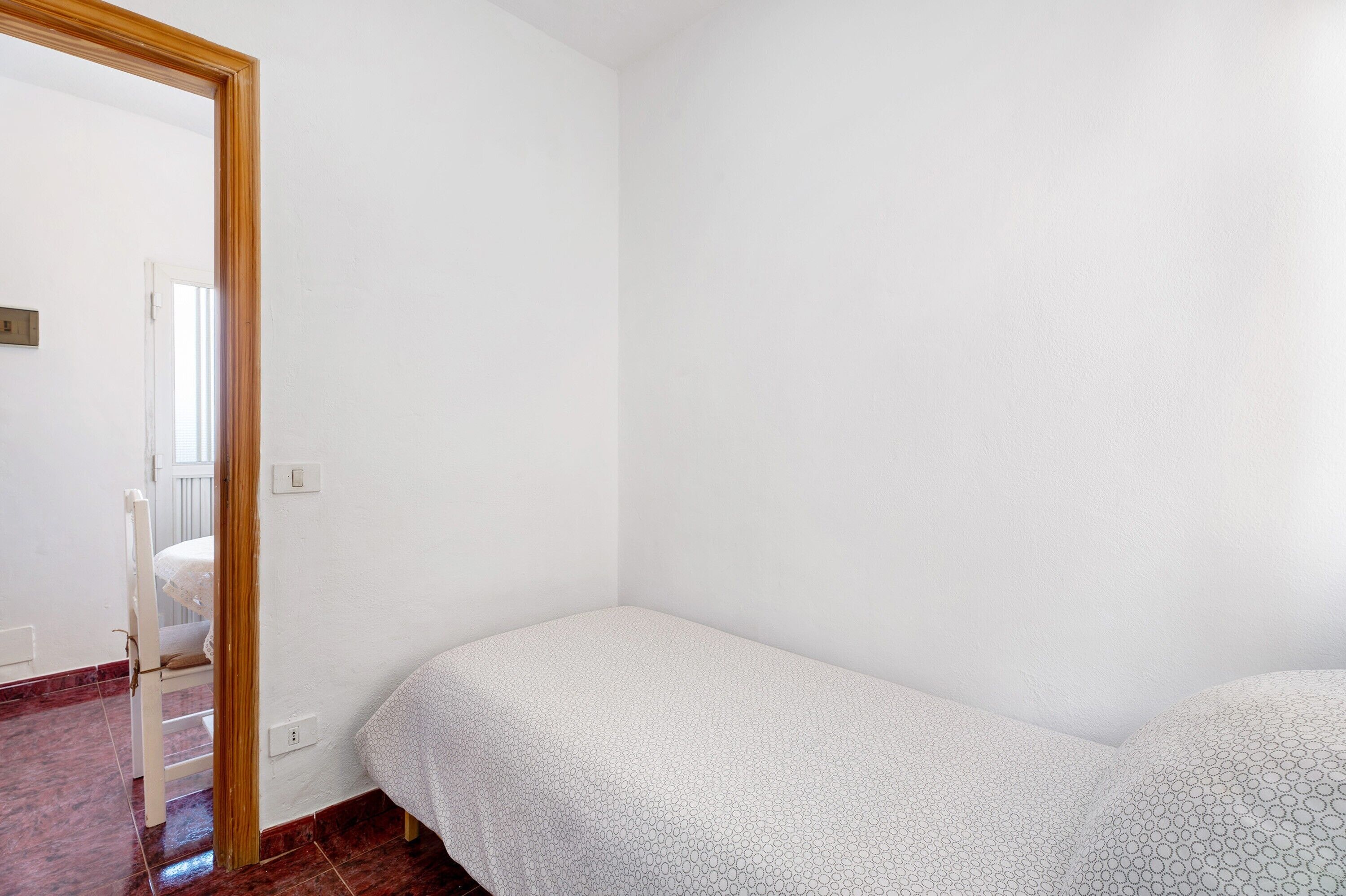 A bedroom with a single bed, a wooden door, and a white wall.