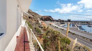 Un balcon offrant une vue sur un port de plaisance, une colline rocheuse et une route menant à des bâtiments.