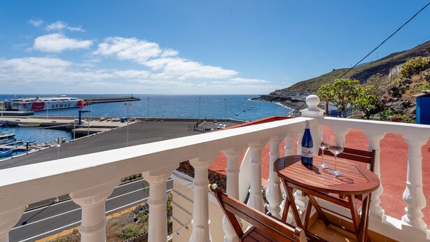 Un balcon avec vue sur la mer, une table avec des chaises et une bouteille de vin.