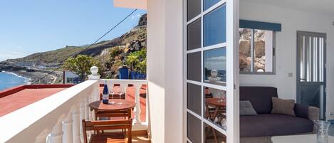 Uma varanda com mesa e cadeiras, um sofá e vista para a costa.