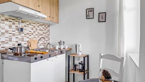 A compact kitchen with a stove, sink, and wooden cabinets. There are two framed artworks on the wall and a small table with a jar of pinecones. - Studio Apartment 'With Sea View' with Sea View, Wi-Fi and Air Conditioning (Drimonas)