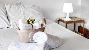 A neatly made bed with white linens, a basket of folded towels, and a bedside table with a lamp. - Studio Apartment 'With Sea View' with Sea View, Wi-Fi and Air Conditioning (Drimonas)
