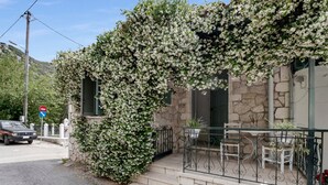 A stone building with a covered porch, a car parked on the street, and a no parking sign. - Studio Apartment 'With Sea View' with Sea View, Wi-Fi and Air Conditioning (Drimonas)