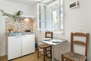 Eine kompakte Küche mit gefliestem Spritzschutz, einem fest eingebauten Herd und einem Fenster mit Vorhängen.