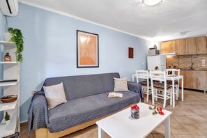 Una sala de estar moderna con un sofá gris, una mesa de centro blanca y un comedor con sillas y una mesa blancos.