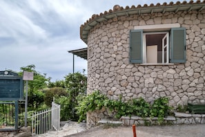Una cabaña de piedra con ventana y contraventanas, una reja de metal y un cartel.