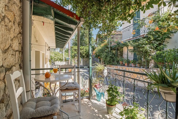 A balcony with a table and chairs, potted plants, and a view of the street.