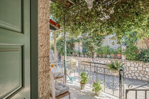 A balcony with a stone wall, potted plants, and a table with a cushion. - Studio Apartment 'Kerkis Mountain View' with Mountain View, Wi-Fi and Air Conditioning (Lefkada)