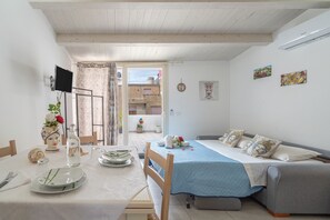 A room with a bed, a sofa, a dining table with plates and a bottle, and a TV.