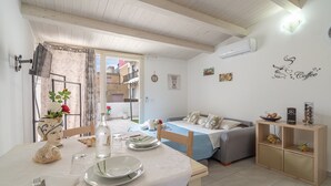 Une pièce comprenant une table à manger dressée pour deux personnes, un canapé, un meuble en bois et un climatiseur fixé au mur.