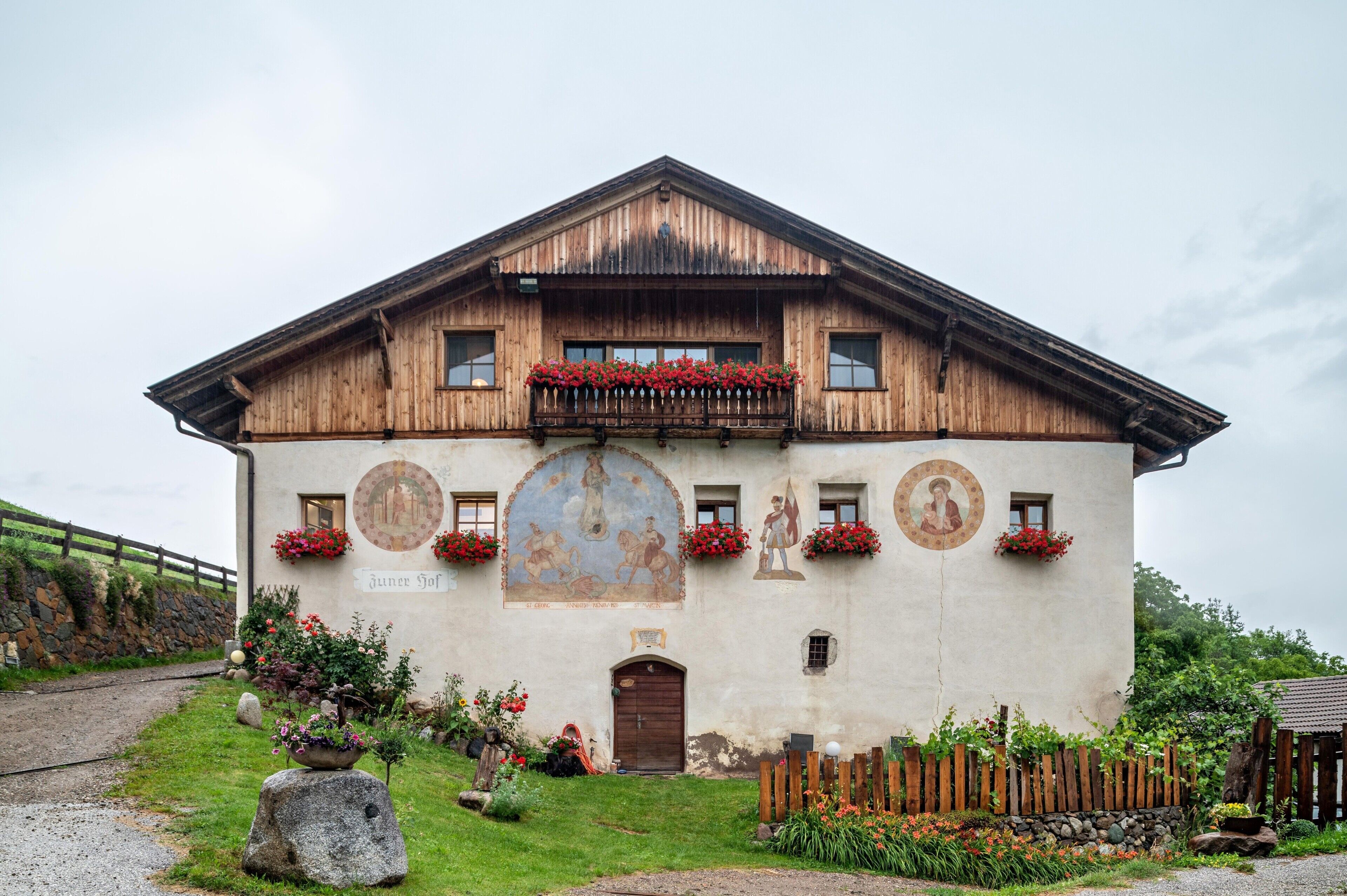 Un edificio tradicional de madera con un balcón, un mural y macetas con flores.