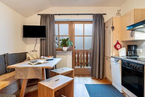 Een knus woongedeelte met een bank, een eettafel, een keuken met fornuis en oven, en een aan de muur bevestigde televisie.