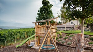 Una estructura de juego de madera con un tobogán y un columpio colgante en un jardín ajardinado.