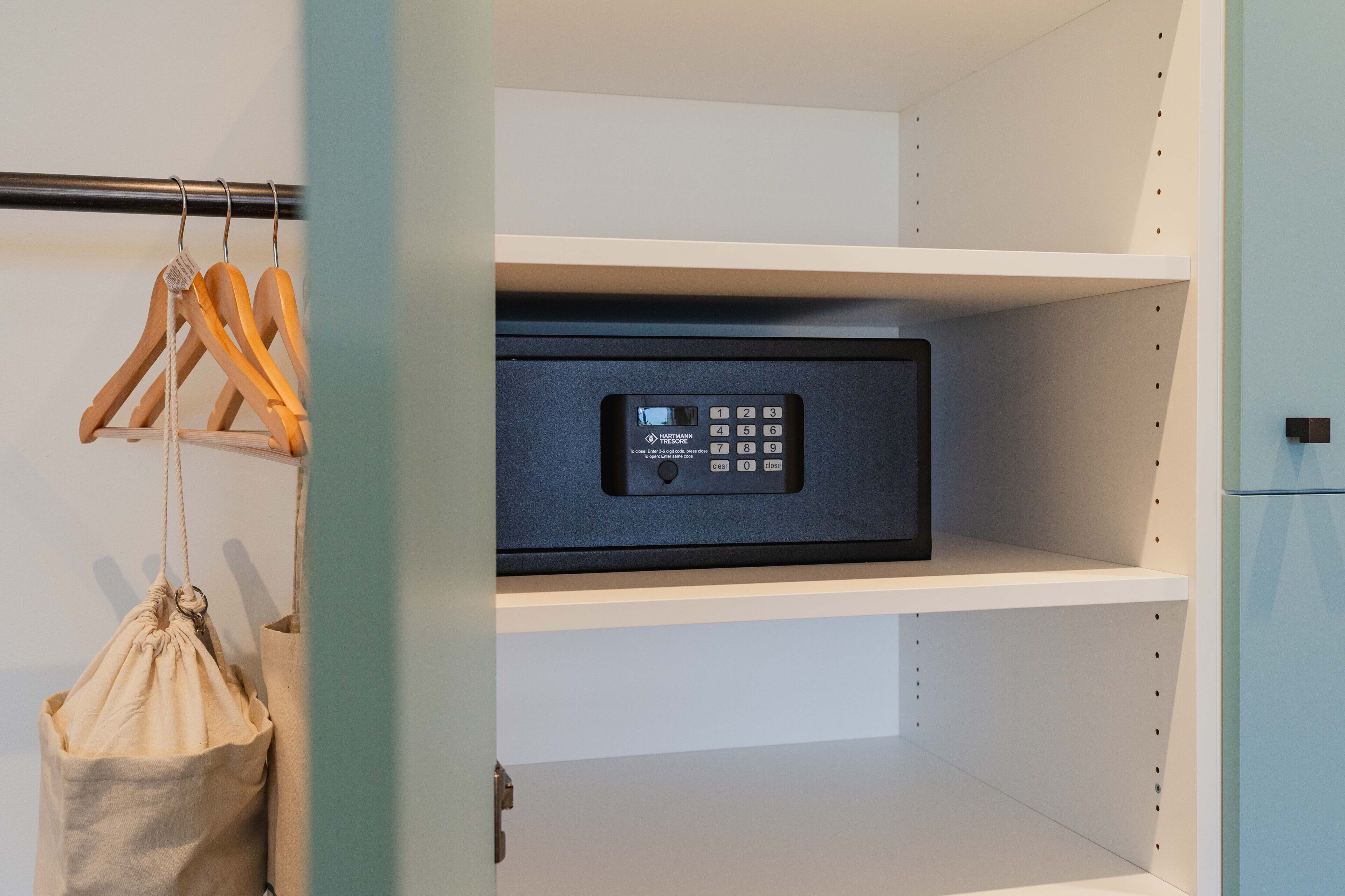 A secure storage unit with a keypad lock, a hanging garment bag, and wooden hangers on a metal rod.