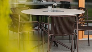 Une table ronde avec des chaises, une bouteille et des verres, sur une terrasse offrant une vue sur les montagnes.