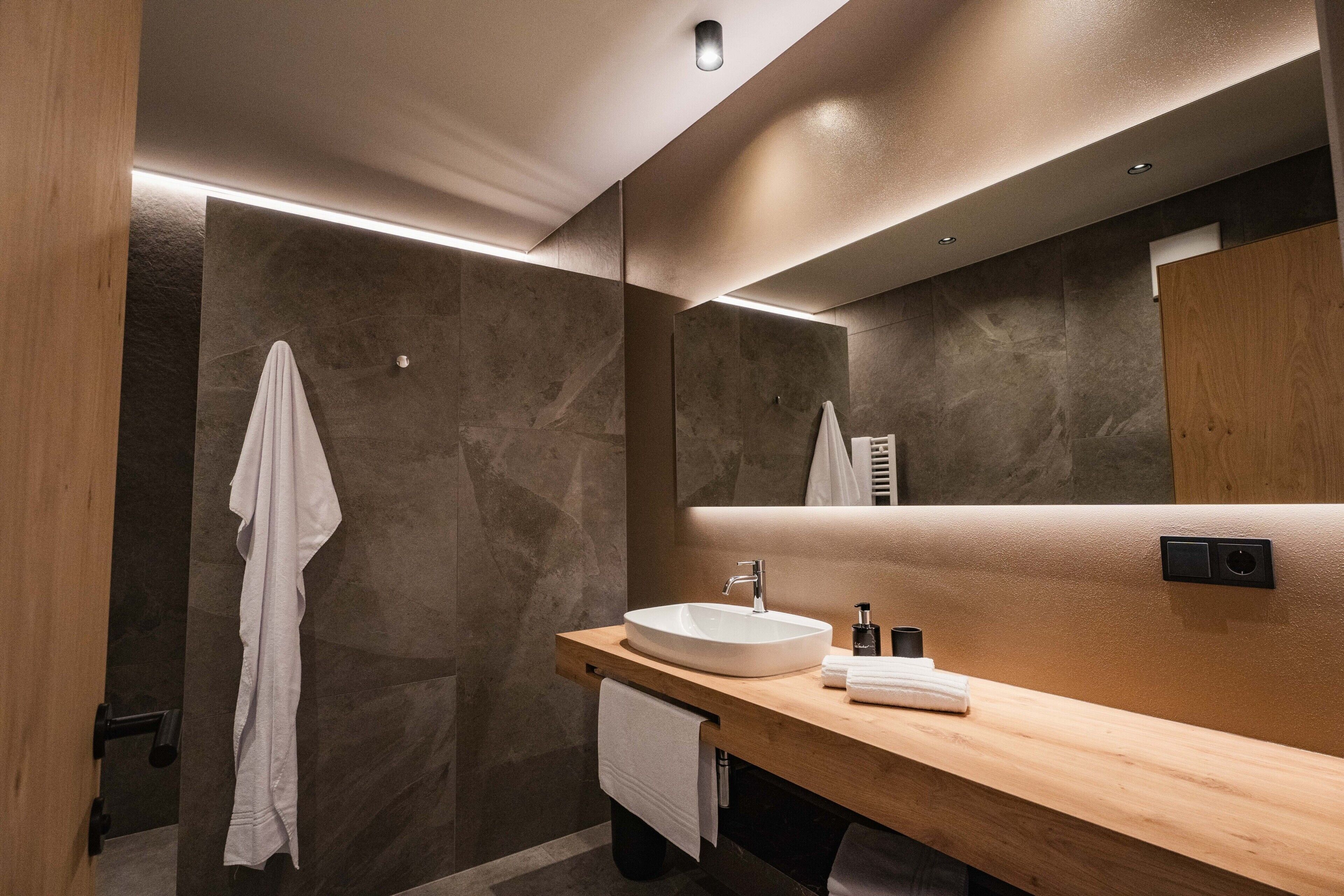 Ein modernes Badezimmer mit einem Holzlagerfläschchen, einem weißen Waschbecken und einem großen Spiegel.