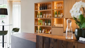 Cozinha moderna com armários de madeira, garrafas de vinho e copos. Há uma área de jantar com cadeiras e uma mesa.