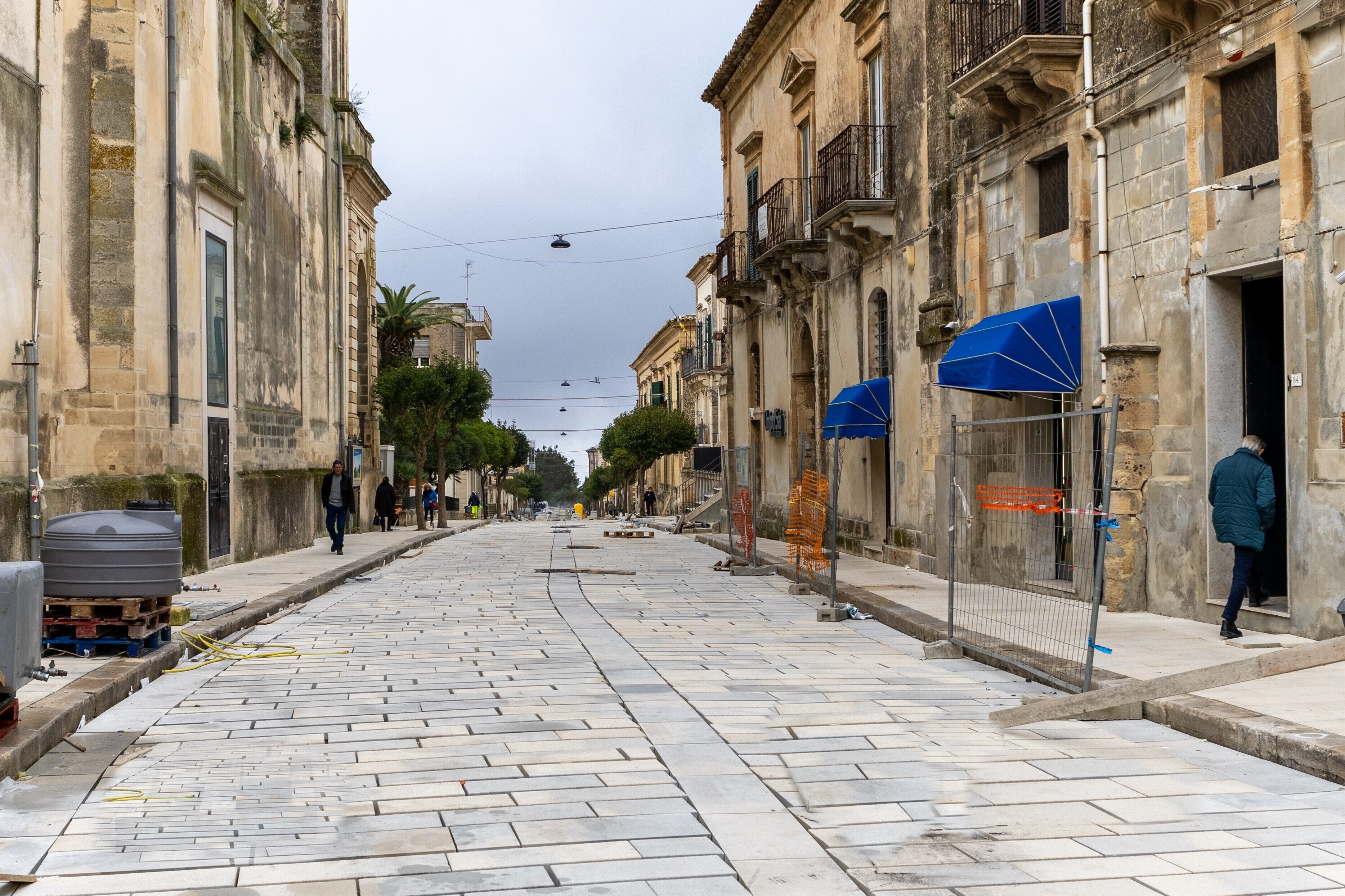 A street with historic buildings, a tiled pavement, and a blue umbrella.