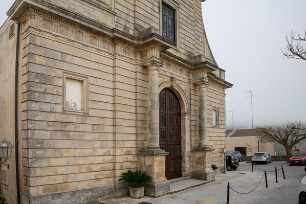 A stone building with a large arched entrance, a potted plant, and a chain barrier.
