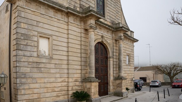 Un edificio de piedra con un amplio acceso en arco, una planta en maceta y una barrera de cadena.