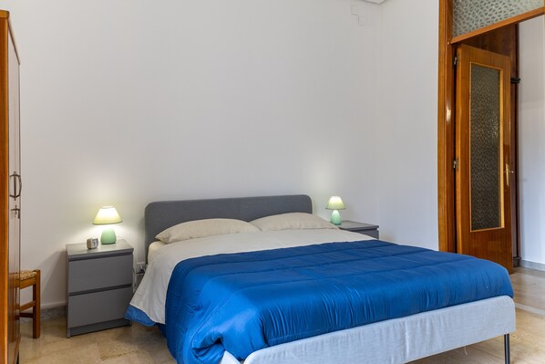 A bedroom with a bed, two bedside tables with lamps, a wooden door, and a small chair.