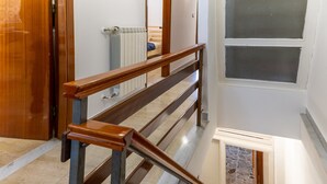 Una escalera de madera con barandilla, un radiador y una ventana con vista a un muro de piedra.