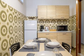 A dining area with a table set for four, a microwave, a refrigerator, and a wooden cabinet above the counter.