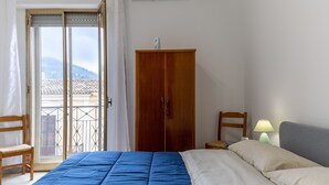 Un dormitorio con cama, armario, silla, lámpara y vistas al exterior.