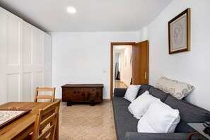 Une pièce comprenant une table à manger en bois, un canapé avec des coussins blancs, un meuble en bois et un tableau encadré accroché au mur.