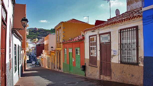 Una calle estrecha con edificios coloridos, cielo despejado y una colina distante.