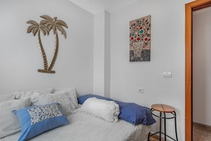 A bedroom with a bed, pillows, a wall art piece, and a small stool.