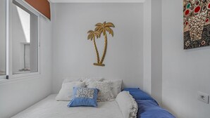 A bedroom with a bed, pillows, a wall art piece of two palm trees, a window, and a wall with a mosaic pattern.