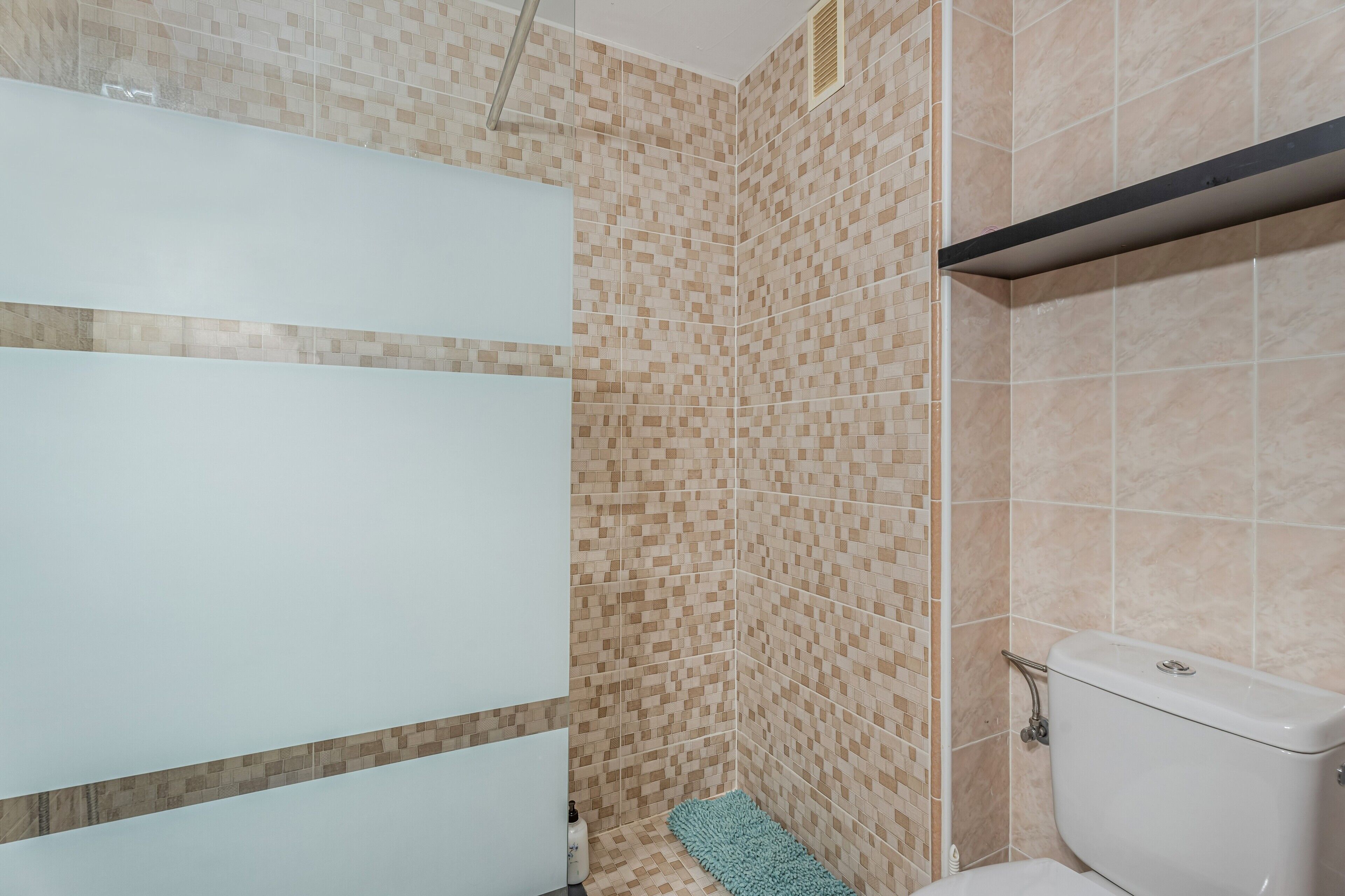 A bathroom with a toilet, a shower, and a tiled wall.