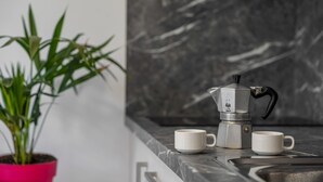 A kitchen counter with a coffee maker, two cups, and a potted plant.