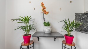A room with a grey table, two potted plants on stools, a white vase with a plant, and a marble wall.