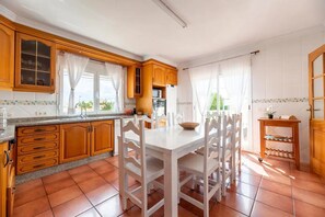 A kitchen with wooden cabinets, a white dining table, and a tiled floor.