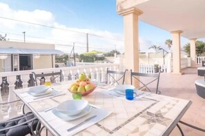 A dining area with a table set for two, a bowl of fruit, and outdoor seating.