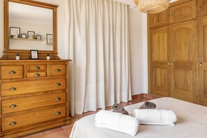 A bedroom with a wooden dresser, a large mirror, a bed with white linens, and a wooden wardrobe.