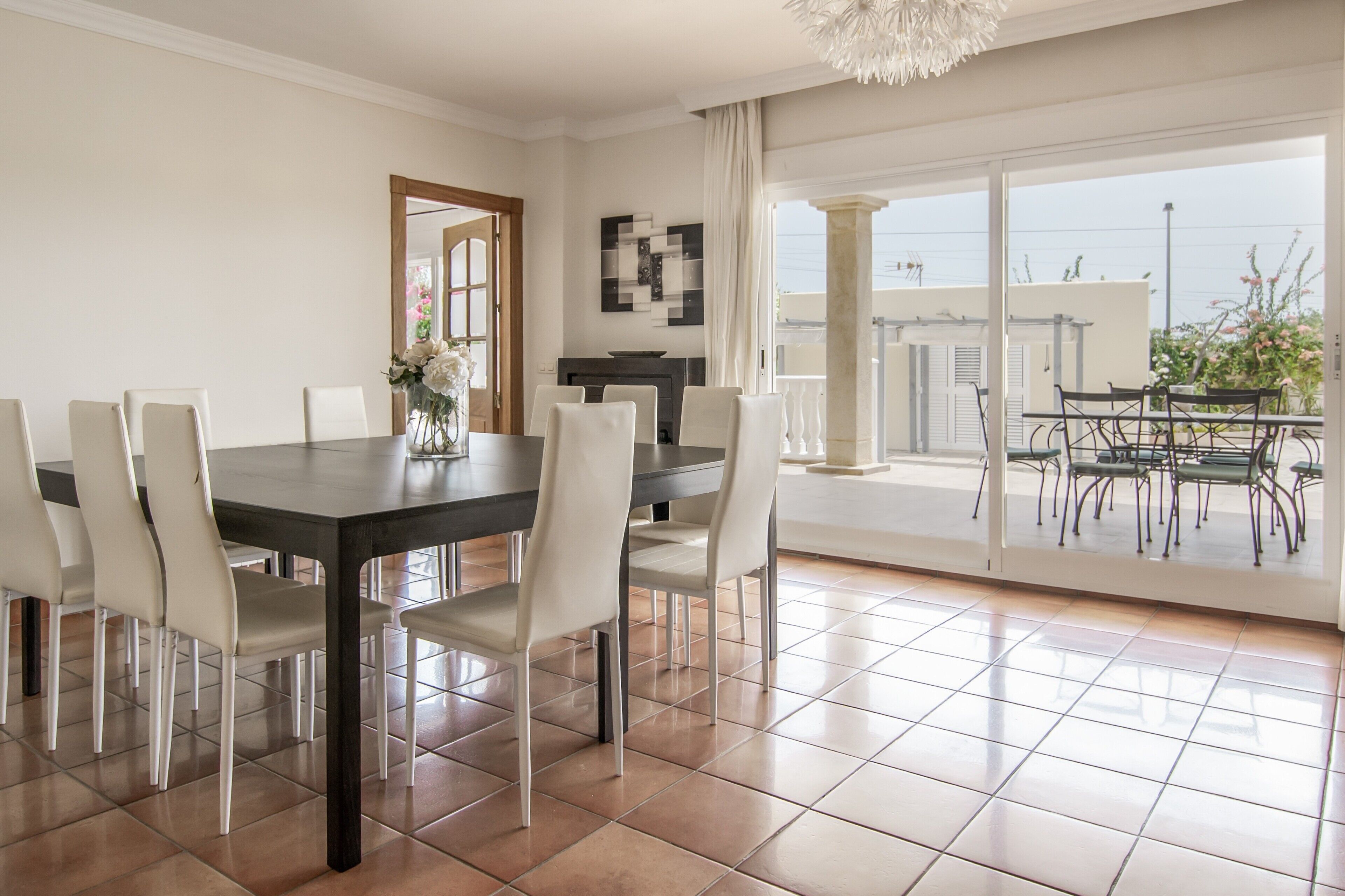 A dining area with a large table, chairs, and a vase of flowers.